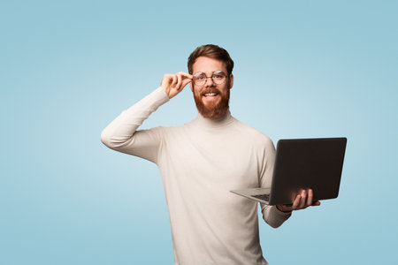 Happy Bearded Man Holding a Laptop Against a Blue Backgroundの写真素材