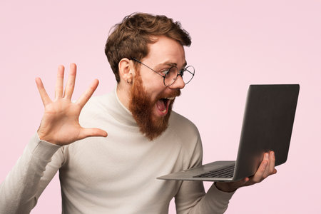 Excited Young Man Engaging Online with Laptop Against Pink Backgroundの写真素材