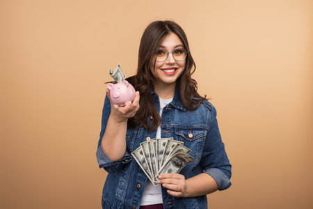 Young Woman Saving Money Holding Piggy Bank and Cash with a Smileの写真素材