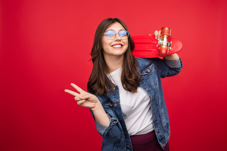 Young Woman Smiling With a Red Skateboard on a Bright Red Backgroundの写真素材