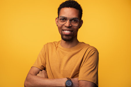 Confident Young Man Smiling in Stylish Glasses Against Yellow Backgroundの写真素材