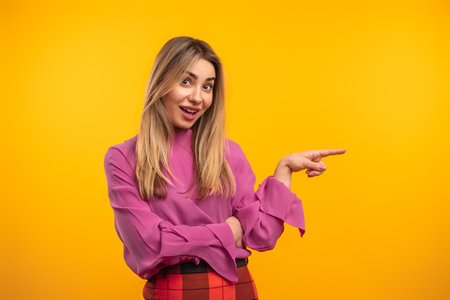 Young Woman in Stylish Outfit Pointing and Smiling Against Yellow Backgroundの写真素材