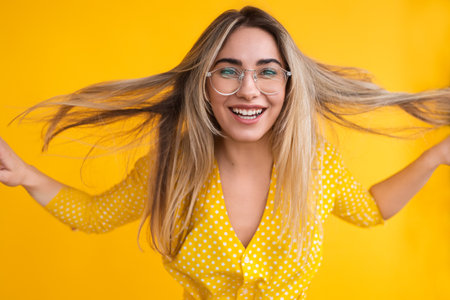 Cheerful Woman With Long Hair Posing Against Yellow Backgroundの写真素材
