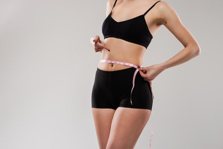 Woman Measuring Waist with Tape in Athletic Wear for Fitness Goalsの写真素材