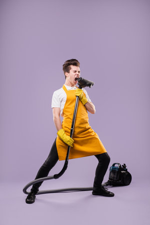 Man Singing With a Vacuum in Fun Cleaning Mood on Purple Backgroundの写真素材