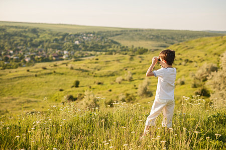 Young Boy Using Binoculars to Explore the Scenic Green Landscapeの写真素材