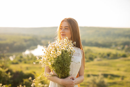 Young Woman Holding a Bouquet of Wildflowers in a Sunny Countrysideの写真素材