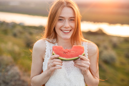 Smiling Redheaded Woman Holding Watermelon in Outdoor Summer Evening Settingの写真素材