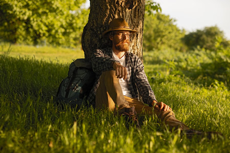 Man Relaxing Against a Tree in Sunlit Nature During Golden Hourの写真素材