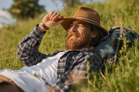 Relaxed Man Lying on Grass in Sunshine Wearing Hat and Checkered Shirtの写真素材