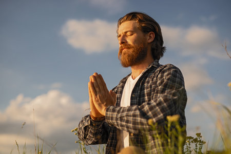 Man Meditating Outdoors with Hands in Prayer Pose at Golden Hourの写真素材