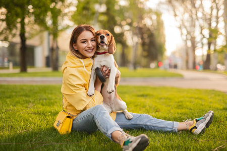 Young Woman Smiling With Her Dog Sitting on the Grass in a Parkの写真素材