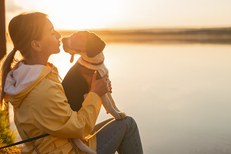 Woman Enjoying Peaceful Moment With Dog by the Lake at Sunsetの写真素材