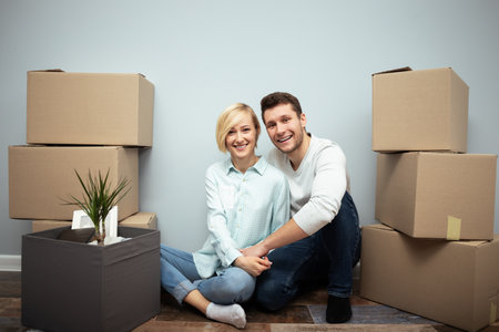 Happy Couple Sitting Among Moving Boxes in Their New Apartmentの写真素材