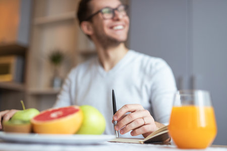 Man Enjoying Healthy Breakfast with Fruits and Orange Juice in Home Settingの写真素材