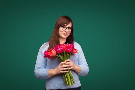 Smiling Woman Holding Pink Tulips Against a Green Backgroundの写真素材