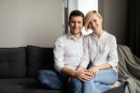 Smiling Couple Sitting Close Together on Comfortable Sofa at Homeの写真素材