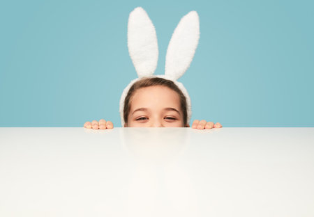 Playful girl in bunny ears hiding behind tableの写真素材
