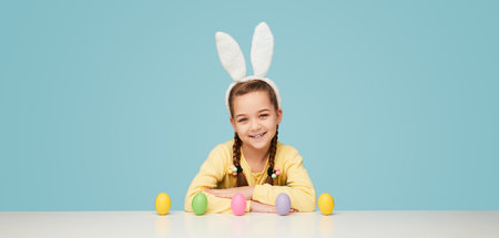 Excited girl celebrating Easter sitting with eggs at tableの写真素材