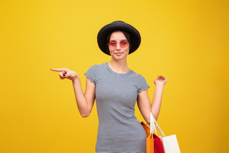Young Stylish Woman with Shopping Bags Posing Against Yellow Backgroundの写真素材