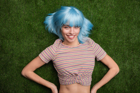 Smiling Woman With Blue Hair Relaxing on Green Grass in a Colorful Outfitの写真素材