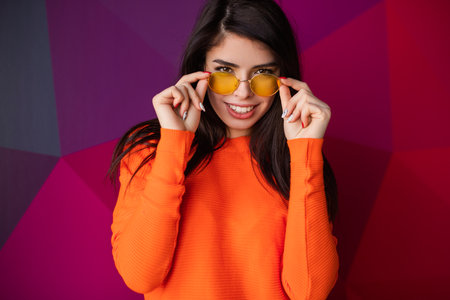 Smiling Woman in Orange Sweater With Yellow Glasses on Vibrant Backgroundの写真素材