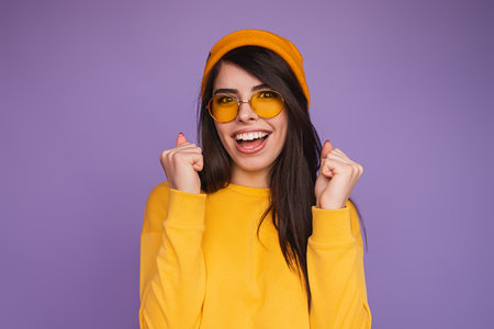 Joyful Woman in Yellow Outfit Celebrating Excitedly Against Purple Backgroundの写真素材