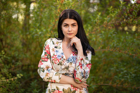 Elegant Woman in Floral Dress Posing in Vibrant Outdoor Settingの写真素材