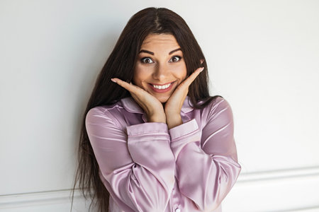 Cheerful Woman Smiling in Satin Pajamas With Hands Framing Her Faceの写真素材