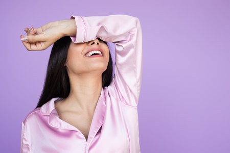 Cheerful Woman Relaxing in Pink Pajamas Against a Pastel Purple Backgroundの写真素材