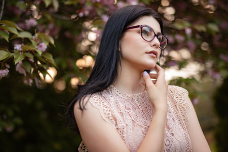 Elegant Woman With Glasses Posing Near Cherry Blossom Trees Outdoorsの写真素材
