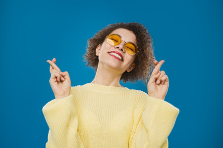 Cheerful Woman Crossing Fingers for Good Luck Wearing Yellow Sweater