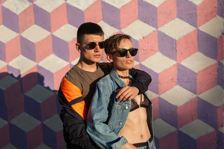 Fashionable Couple in Sunglasses Posing Against Colorful Geometric Wall Artworkの写真素材
