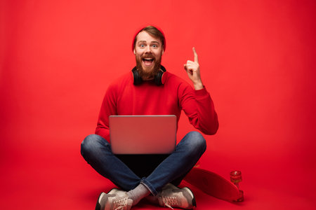 Excited Man in Red Using Laptop Against Vibrant Red Backgroundの写真素材
