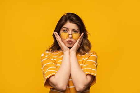 Playful Young Woman in Yellow Sunglasses and Matching Vibrant Backgroundの写真素材