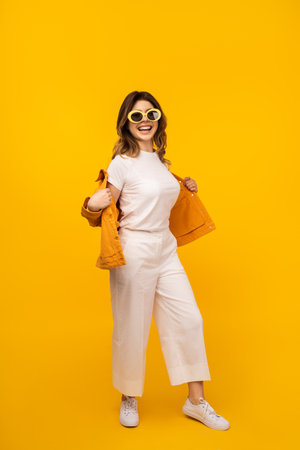 Cheerful Woman in Fashionable Outfit Against Bright Yellow Backgroundの写真素材