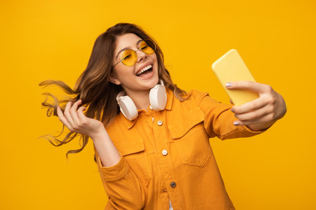 Cheerful Woman Taking a Vibrant Selfie With a Bright Yellow Backgroundの写真素材