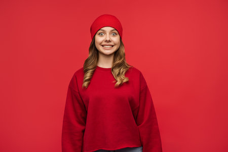 Young Woman in Red Beanie Smiling Against Bright Red Backgroundの写真素材