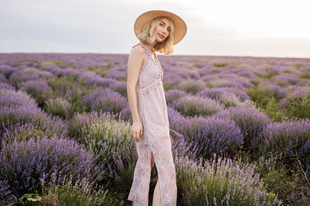 Woman Enjoying Lavender Field Scenery in Elegant Summer Dress and Straw Hatの写真素材
