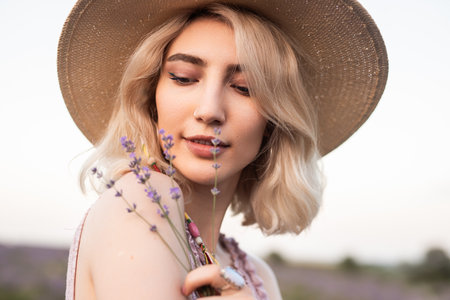 Woman in a Hat Holding Lavender in a Serene Outdoor Settingの写真素材
