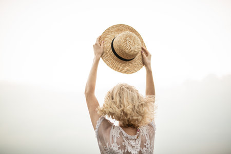 Woman Holding a Straw Hat Outdoors in Sunlit Natureの写真素材