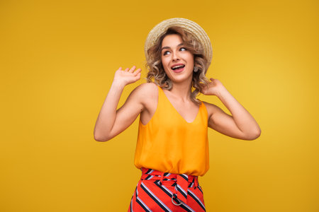 Cheerful Young Woman Wearing Yellow Top and Straw Hat on Yellow Backgroundの写真素材