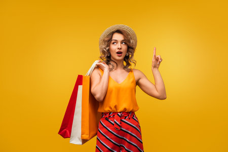 Excited Woman Holding Shopping Bags With Finger Pointing Up on Yellow Backgroundの写真素材