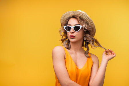 Stylish Woman in Summer Attire Posing Against Vibrant Yellow Backgroundの写真素材