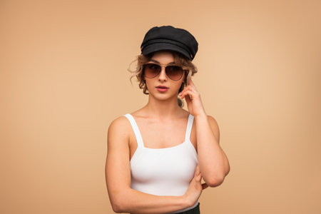 Fashionable Woman Wearing Sunglasses and Cap Posing Against a Neutral Backgroundの写真素材