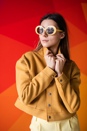 Stylish Woman Posing in Yellow Jacket with Sunglasses Against Vibrant Backgroundの写真素材