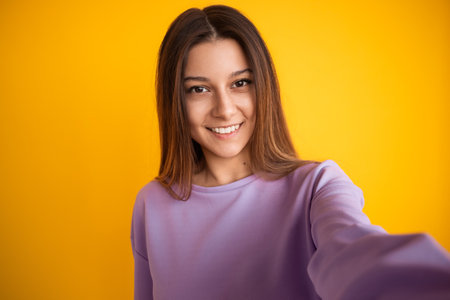 Young Woman Smiling in Violet Top Against Bright Yellow Backgroundの写真素材