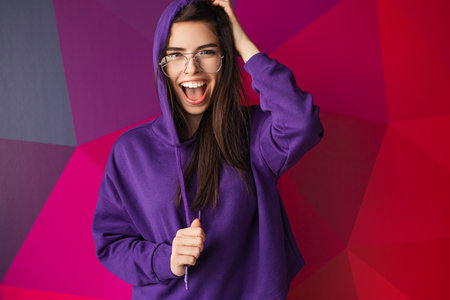 Joyful Woman in Purple Hoodie With Vibrant Geometric Backgroundの写真素材