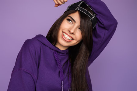 Smiling Young Woman in Purple Hoodie and Backwards Cap Against Lavender Backgroundの写真素材
