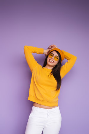 Happy Young Woman in Stylish Yellow Outfit Posing Against Purple Backgroundの写真素材